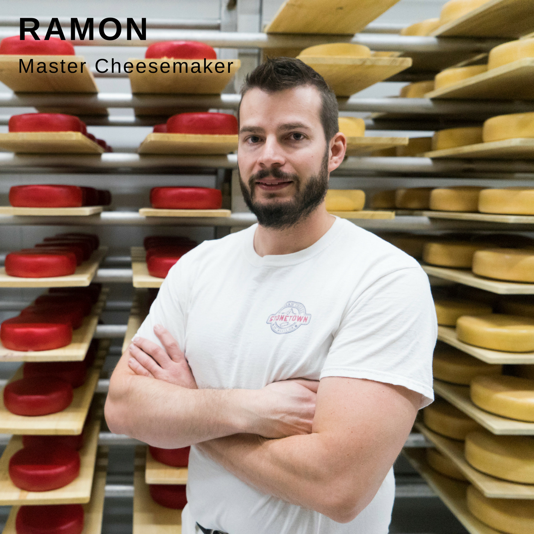 Man smiling while standing in front of wheels of cheese